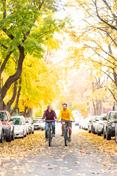 两个学生 ride down Greek Row in the fall, amid changing leaves.